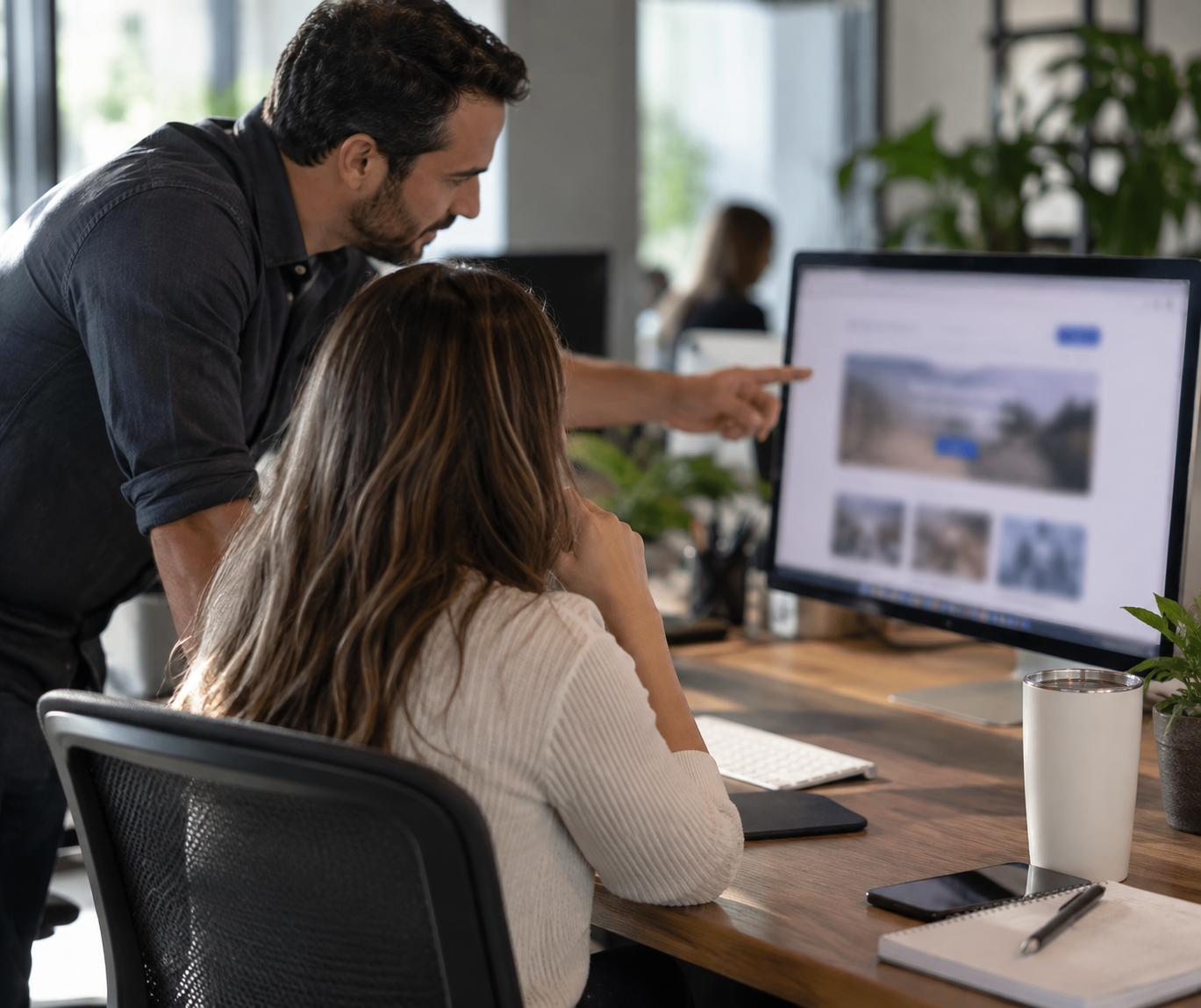 Two digital marketing professionals reviewing a business homepage on a large monitor in a modern office.